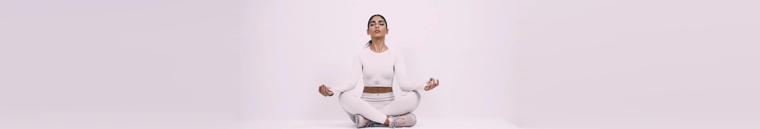 A model in white Aliens Fit activewear seated cross-legged against a pale studio background