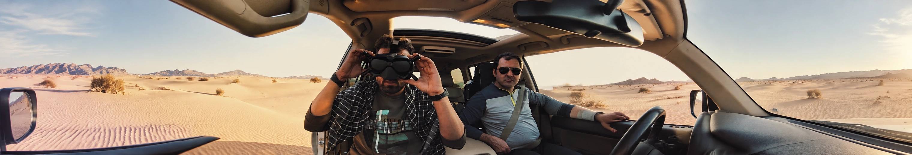 An FPV pilot wearing goggles beside a driver in a desert vehicle