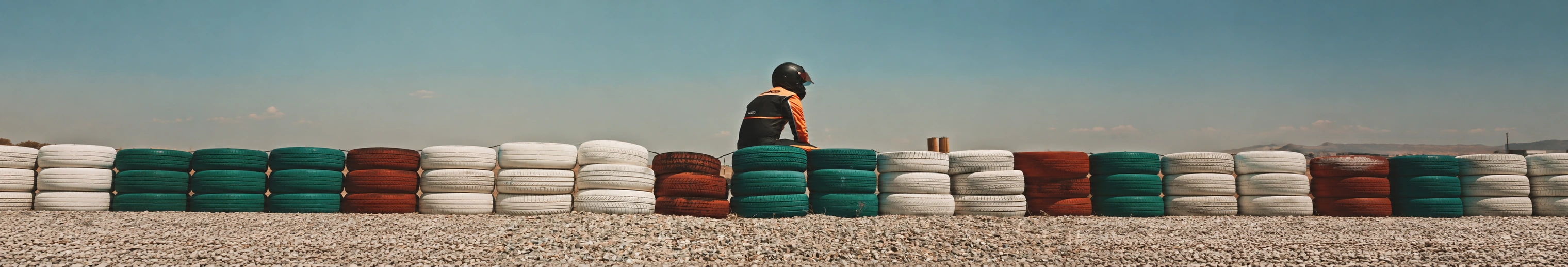 A helmeted karting driver behind a colorful tyre barrier at the track